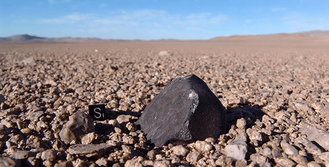 Condrito Carbónaceo encontrado en el desierto de Atacama por R. Martinez (Museo del Meteorito). Formados en asteroides ricos en carbono, este grupo de meteoritos trae complejos componentes orgánicos, que podrían haber originado la vida en la Tierra.